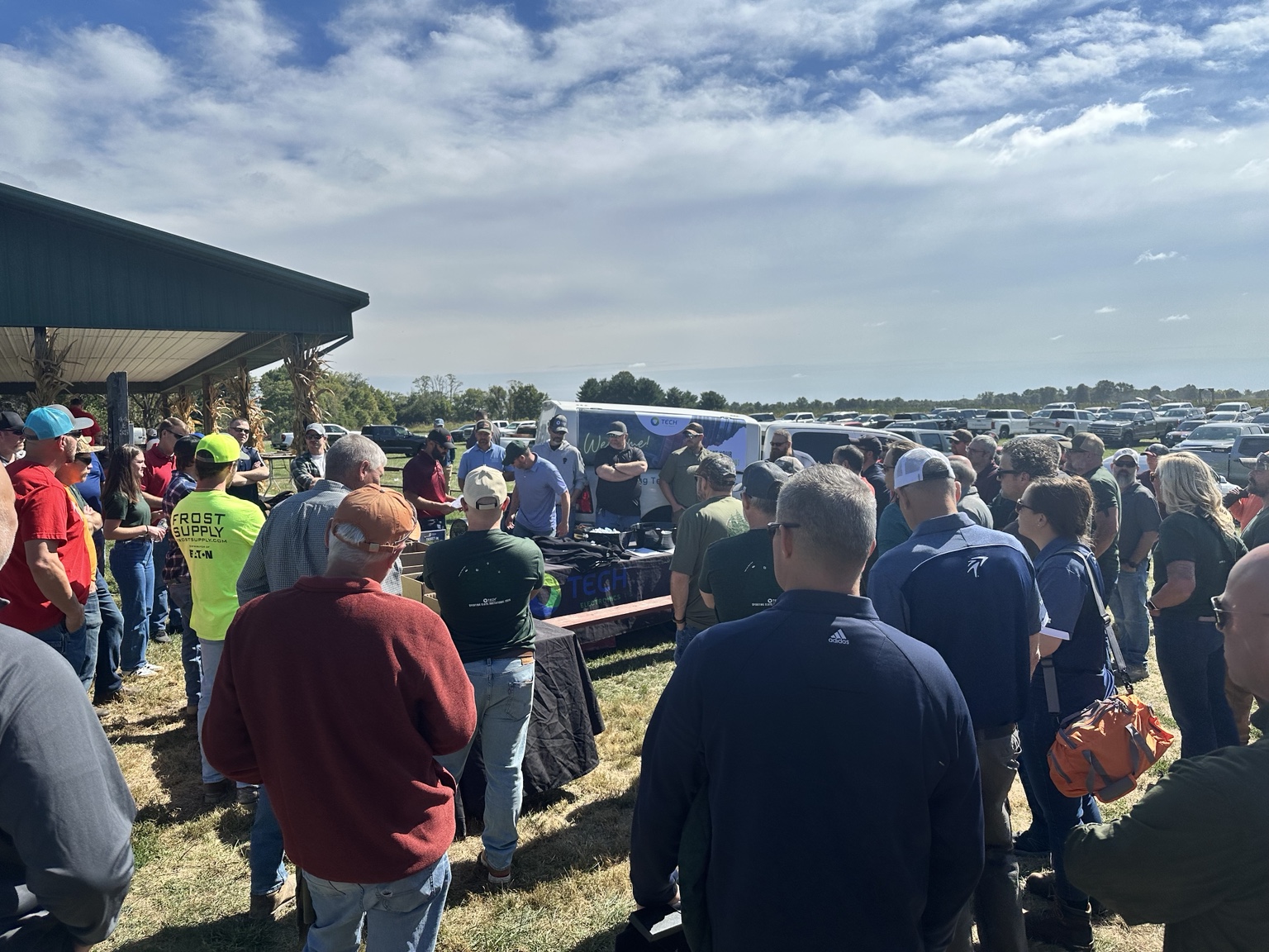 A large NILO Farms event crowd gathered in front of a packed parking area, with green event shirts visible